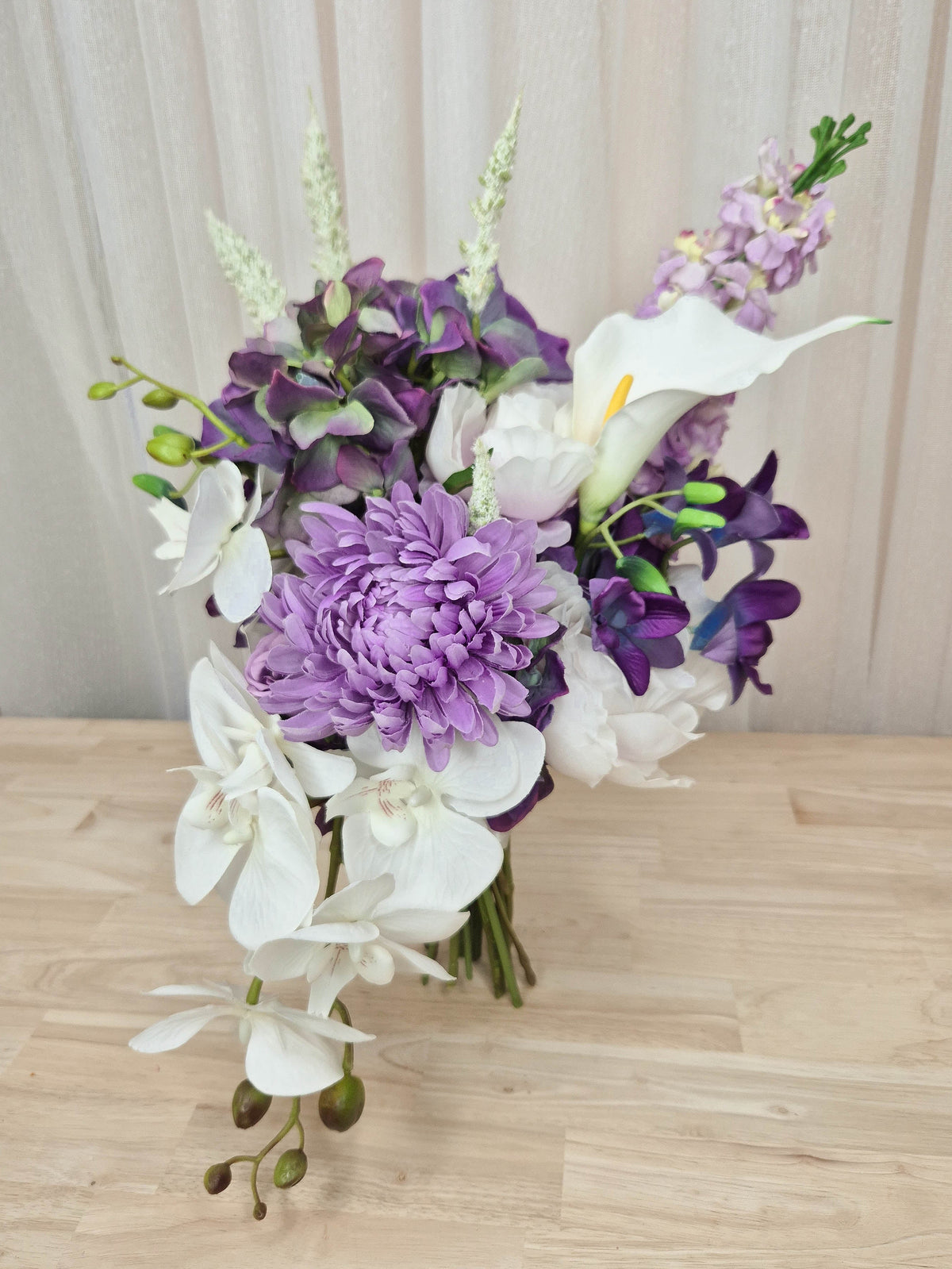 A mixed artificial floral bouquet with purple and white flowers, including a large purple chrysanthemum, white orchids, white calla lilies, and purple delphiniums.  Made in Melbourne Australia, by Australia's best silk bridal florist