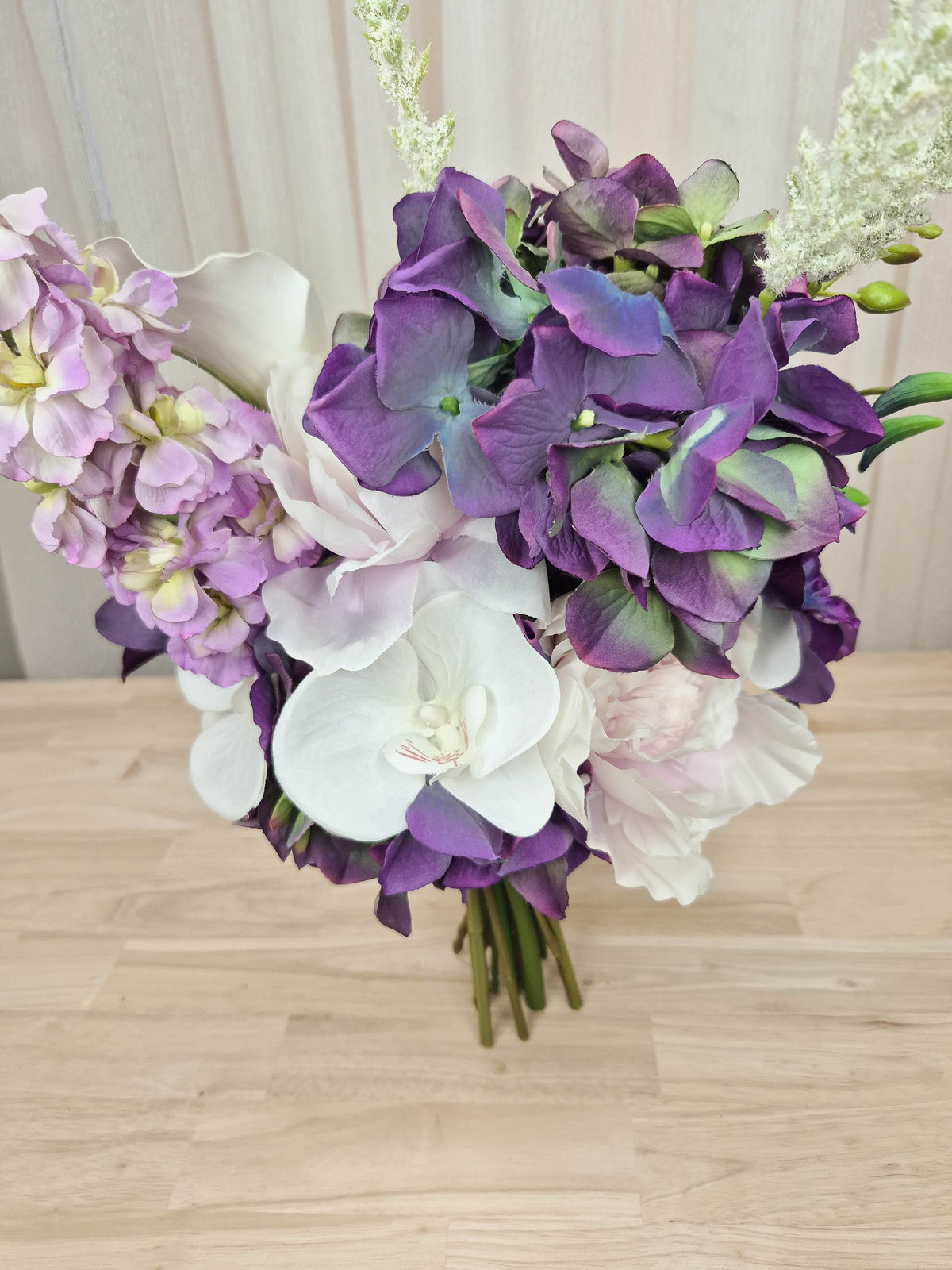 A mixed artificial floral bouquet with purple and white flowers, including a large purple chrysanthemum, white orchids, white calla lilies, and purple delphiniums.  Made in Melbourne Australia, by Australia's best silk bridal florist