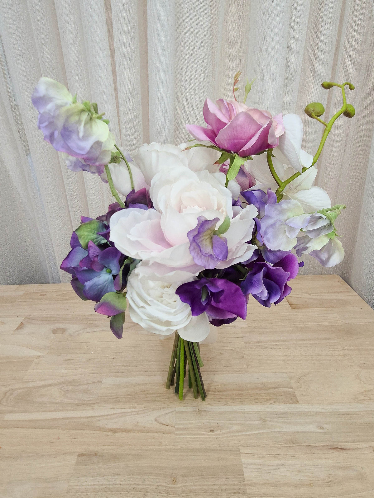 A mixed artificial floral bridesmaid bouquet with purple and white flowers, including lilac roses, purple hydrangea, lilac sweet pea, and orchids.  Made in Melbourne Australia, by Australia's best silk bridal florist