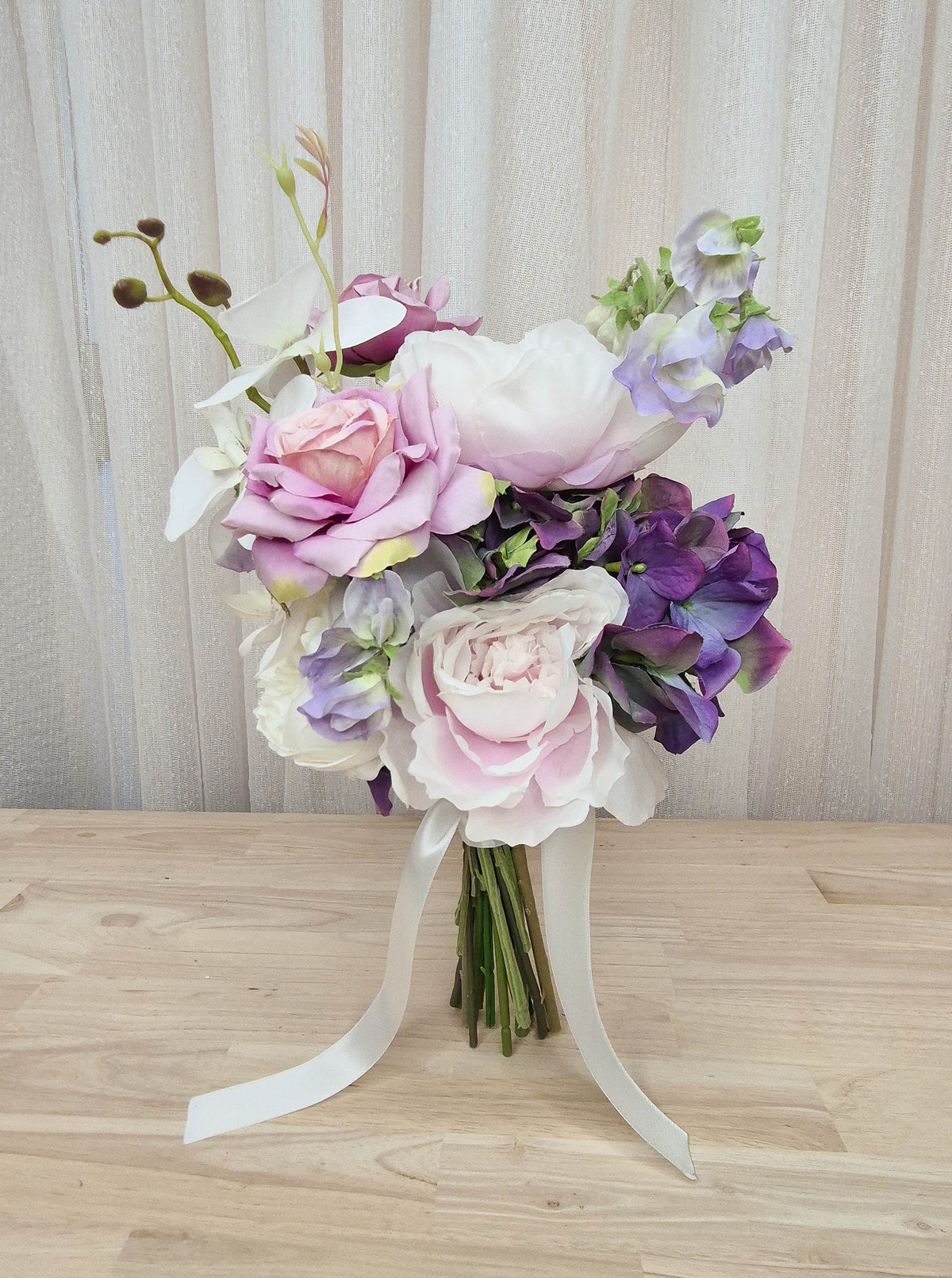 A mixed artificial floral bridesmaid bouquet with purple and white flowers, including lilac roses, purple hydrangea, lilac sweet pea, and orchids.  Made in Melbourne Australia, by Australia's best silk bridal florist