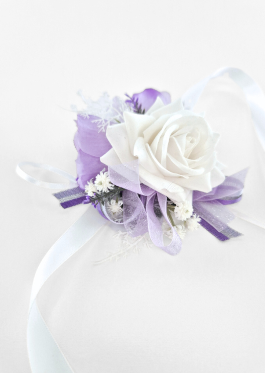 Artificial wedding wrist corsage, angled view of a white faux rose framed by lilac roses, tiny white flowers and lilac ribbons. For formals, proms and ball occasions. Made in Melbourne by Flowers For Ever After, shipping Australia and Worldwide.