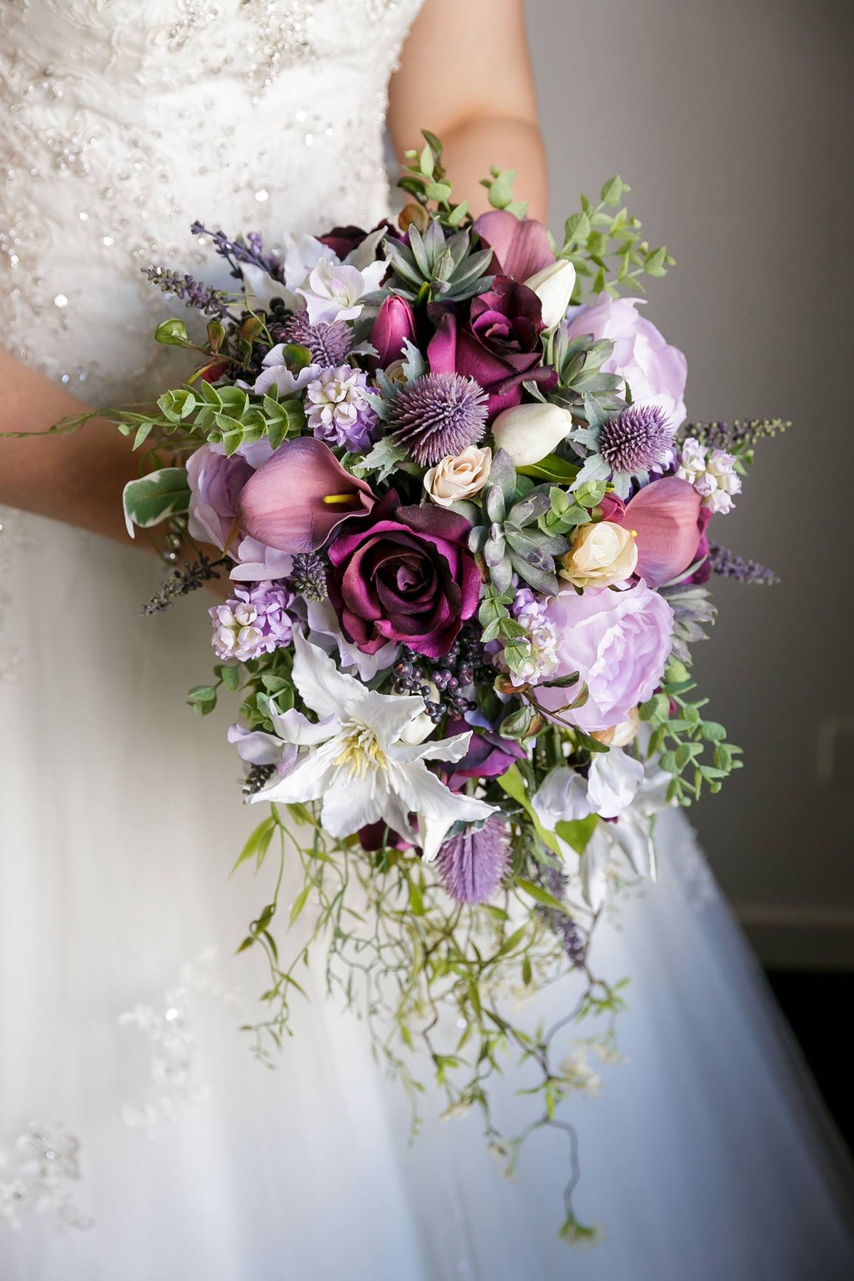 A tear shaped bouquet of artificial purple flowers including call lillies, tulips, roses, peonies and various other garden florals. Flowers by Flowers For Ever After