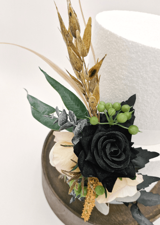 Artificial wedding cake decoration close-up with a black faux rose, cream blooms, green berries and golden sprigs. For birthday, event and celebration cakes. Made in Melbourne by Flowers For Ever After, shipping Australia and Worldwide.