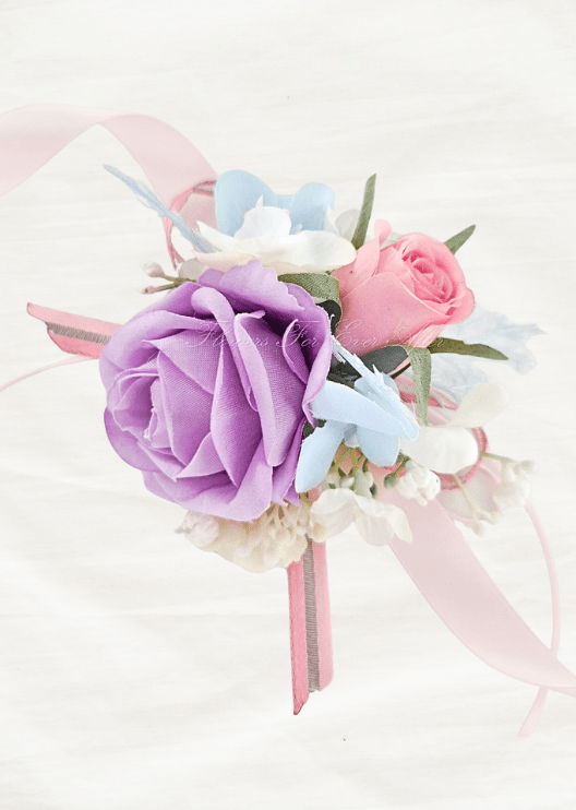 Artificial wedding wrist corsage with lilac and pink faux roses, pale blue and white flowers and pink ribbon tails. For formals, proms and ball occasions. Made in Melbourne by Flowers For Ever After, shipping Australia and Worldwide.