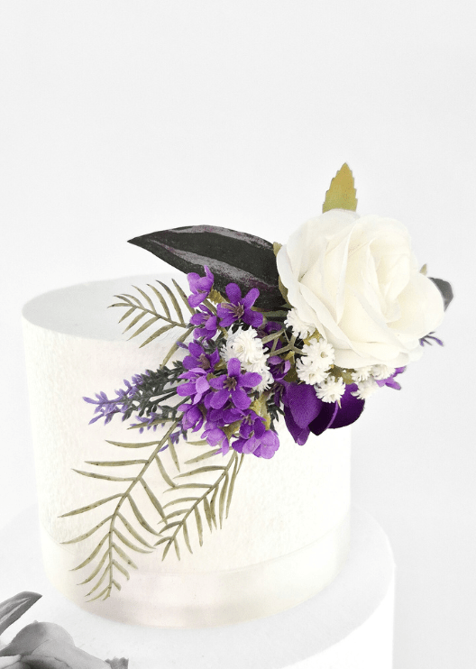 Artificial wedding cake topper close-up with a white faux rose, purple blossoms, tiny white flowers and fern-like leaves. For birthday, event and celebration cakes. Made in Melbourne by Flowers For Ever After, shipping Australia and Worldwide.