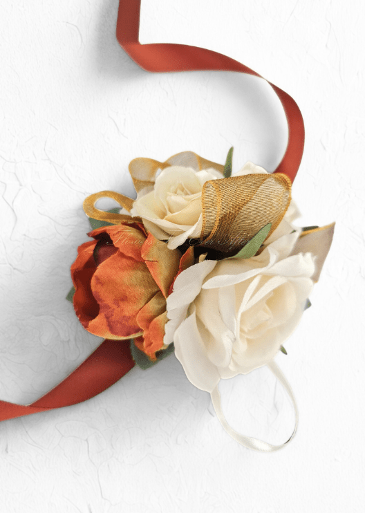 Artificial wedding wrist corsage with rust-orange and cream faux roses, gold ribbon loops and long rust-coloured ribbon ties. For formals, proms and ball occasions. Made in Melbourne by Flowers For Ever After, shipping Australia and Worldwide.