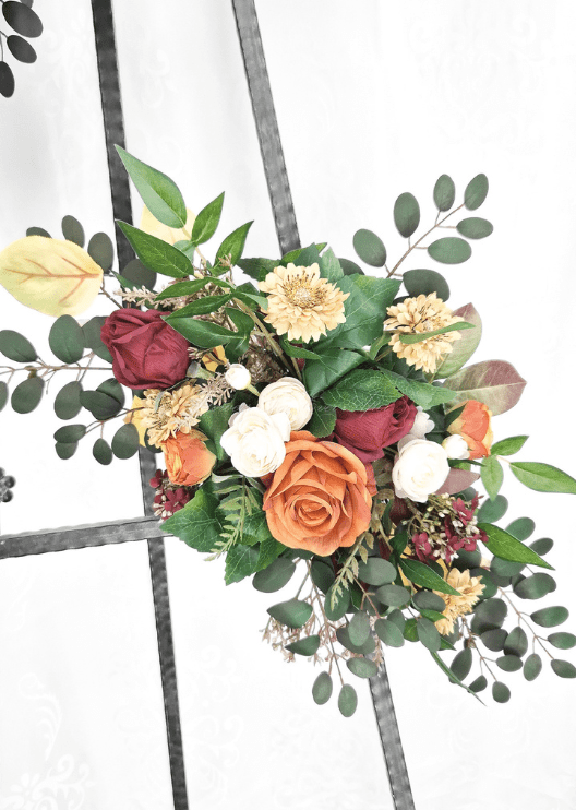 Artificial wedding smaller arbor spray, angled view of a rust faux rose, burgundy rosebuds, golden daisies and eucalyptus. Made in Melbourne by Flowers For Ever After, shipping Australia and Worldwide.