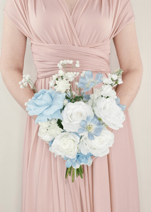 Artificial wedding bridesmaid bouquet held in both hands, with white faux roses, pale blue flowers and small white sprigs. Made in Melbourne by Flowers For Ever After, shipping Australia and Worldwide.