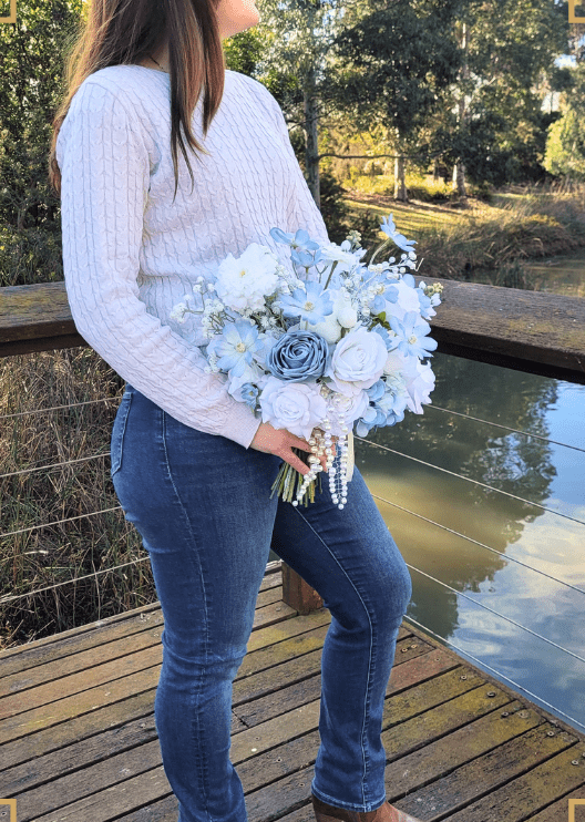 Artificial wedding bridal bouquet held in both hands, with white and dusty blue faux roses, pale blue flowers and pearl strands. Made in Melbourne by Flowers For Ever After, shipping Australia and Worldwide.