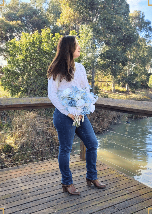 Artificial wedding bridal bouquet held by a woman, with white and dusty blue faux roses, blue flowers and dangling pearl strands. Made in Melbourne by Flowers For Ever After, shipping Australia and Worldwide.