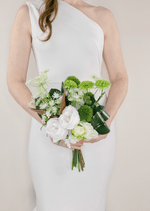Artificial wedding bouquet held by a bride, with white faux roses, lime green blooms, green pompom flowers and dark curled leaves. Made in Melbourne by Flowers For Ever After, shipping Australia and Worldwide.