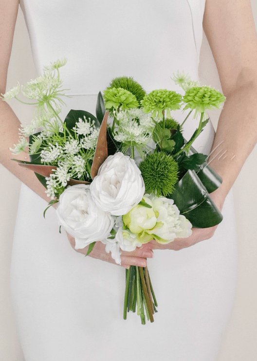 Artificial wedding bouquet held in both hands, with white faux roses, lime green blooms, green pompom flowers and curled dark leaves. Made in Melbourne by Flowers For Ever After, shipping Australia and Worldwide.