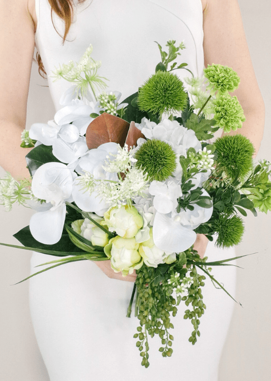 Artificial wedding bridal bouquet held by a bride, with white faux orchids, green pompom blooms, lime green flowers and trailing green buds. Made in Melbourne by Flowers For Ever After, shipping Australia and Worldwide.
