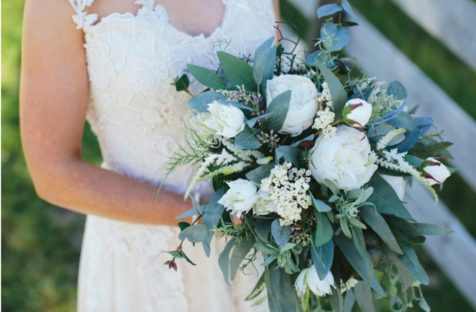 A close up of a rustic cascading faux bridal bouquet featuring white peonies, foliages, proteas and various other textures. Flowers by Flowers For Ever After