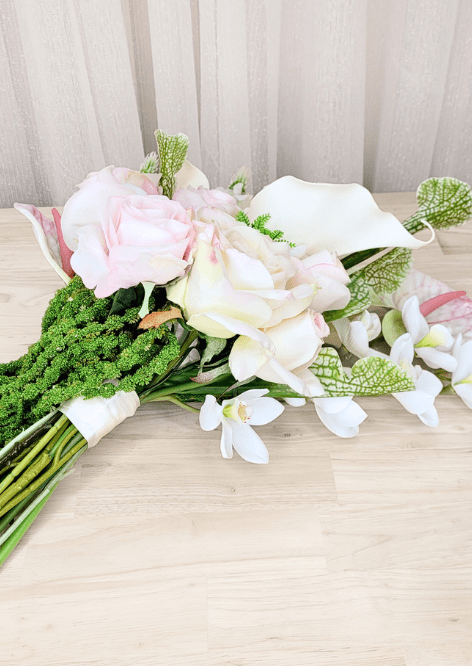Artificial wedding bouquet laid sideways, showing pink and white faux blooms, orchids, gathered stems and trailing green strands. Made in Melbourne by Flowers For Ever After, shipping Australia and Worldwide.