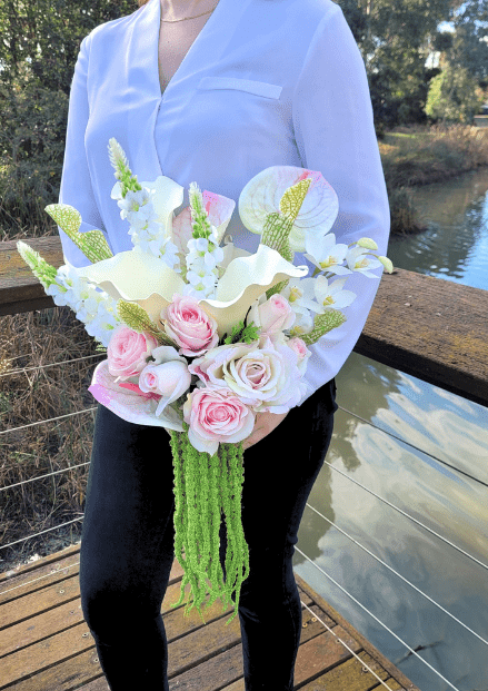 Artificial wedding bouquet held at waist height, closer view of pink and white faux blooms, anthuriums and trailing green strands. Made in Melbourne by Flowers For Ever After, shipping Australia and Worldwide.