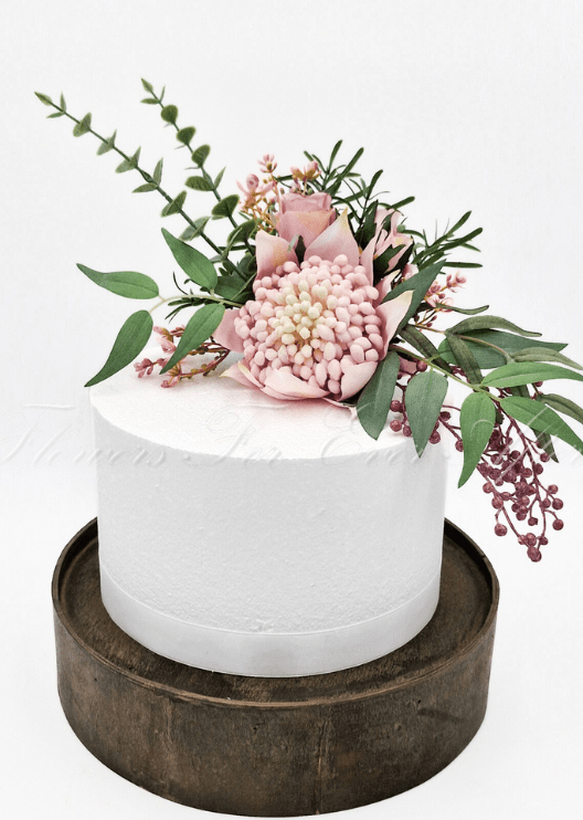 Artificial wedding cake decoration with pink faux waratah, native-style foliage and small filler flowers arranged over the cake tiers. For birthday, event and celebration cakes. Made in Melbourne by Flowers For Ever After, shipping Australia and Worldwide.