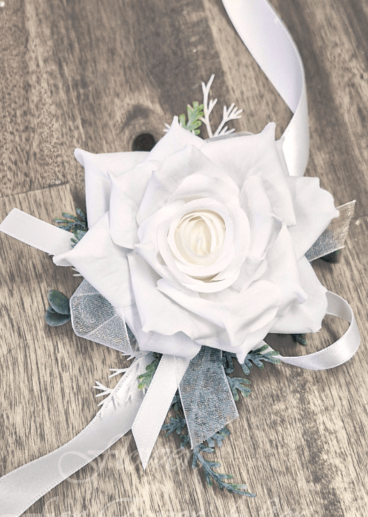 Artificial wedding wrist corsage with a white faux rose, silver sprigs, grey-green leaves and ivory satin and sheer ribbon loops. For formals, proms and ball occasions. Made in Melbourne by Flowers For Ever After, shipping Australia and Worldwide.