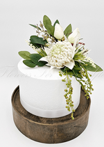 Artificial wedding cake decoration with white faux waratah, small filler blooms and green leaves across the tiers. For birthday, event and celebration cakes. Made in Melbourne by Flowers For Ever After, shipping Australia and Worldwide.