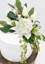 Artificial wedding cake decoration, angled view of white faux waratah blooms and green leaves. For birthday, event and celebration cakes. Made in Melbourne by Flowers For Ever After, shipping Australia and Worldwide.