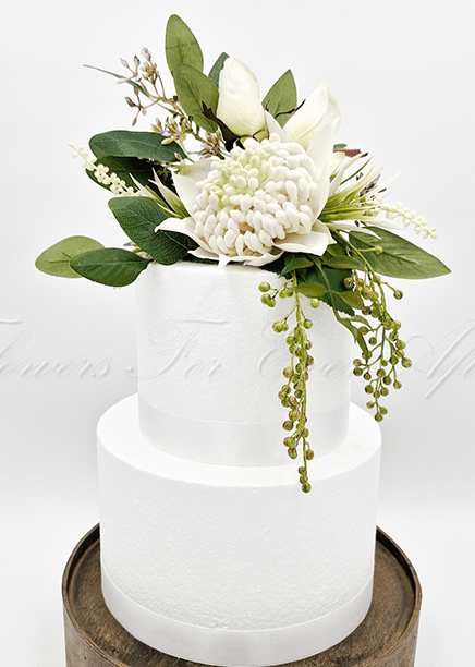 Artificial wedding cake decoration close-up with white faux waratah and green native-style foliage. For birthday, event and celebration cakes. Made in Melbourne by Flowers For Ever After, shipping Australia and Worldwide.