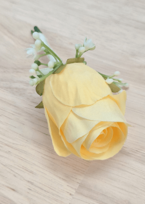 Artificial wedding boutonniere, overhead view of a pale yellow faux rosebud, tiny white flowers and green sepals. For formals, proms and ball occasions. Made in Melbourne by Flowers For Ever After, shipping Australia and Worldwide.