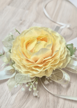 Artificial wedding wrist corsage with a pale yellow faux ranunculus, tiny white sprigs, pale green blossoms and gold-edged ivory ribbons. For formals, proms and ball occasions. Made in Melbourne by Flowers For Ever After, shipping Australia and Worldwide.