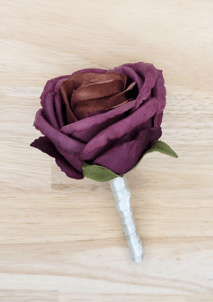 Artificial wedding boutonniere close-up showing plum faux rose petals, green sepals and white-wrapped stem. For formals, proms and ball occasions. Made in Melbourne by Flowers For Ever After, shipping Australia and Worldwide.