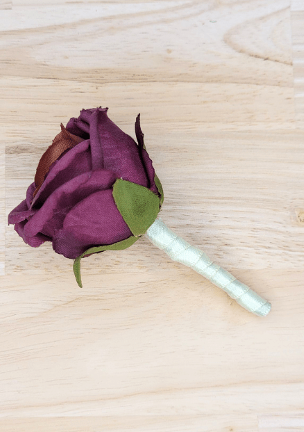 Artificial wedding boutonniere with plum faux rosebud, green sepals and white-wrapped stem, side view. For formals, proms and ball occasions. Made in Melbourne by Flowers For Ever After, shipping Australia and Worldwide.