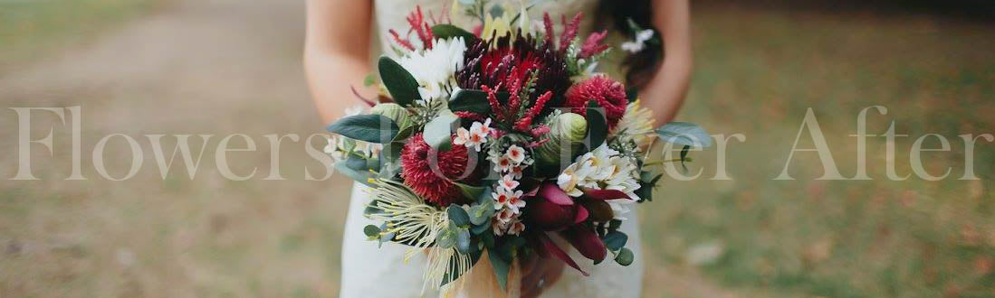 A close-up of a person holding a large, lush faux floral bouquet with deep red, burgundy, white, and green flowers, set against a softly blurred outdoor background. Flowers by Flowers For Ever After