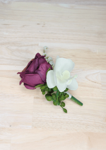 Artificial wedding boutonniere, overhead view of plum faux rosebud, white orchid and green berries. For formals, proms and ball occasions. Made in Melbourne by Flowers For Ever After, shipping Australia and Worldwide.