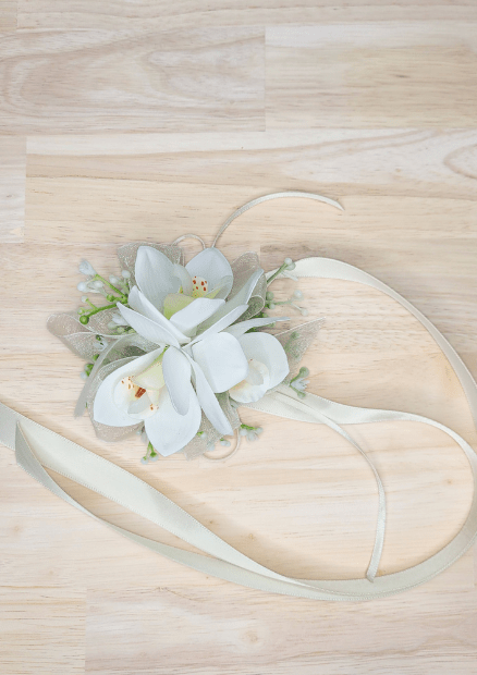 Artificial wedding wrist corsage with white faux orchids, tiny pale buds and long ivory ribbon ties, overhead view. For formals, proms and ball occasions. Made in Melbourne by Flowers For Ever After, shipping Australia and Worldwide.